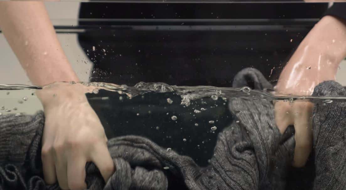 woman scrubbing grey sweater in large tub full of water
