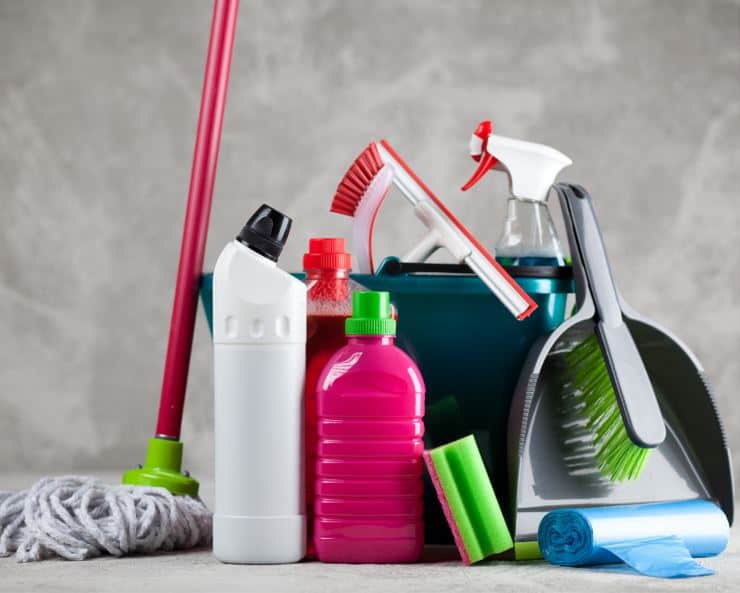 assorted cleaning tools and equipment on the floor including a mop, dustpan, bucket and various coloured spray bottles