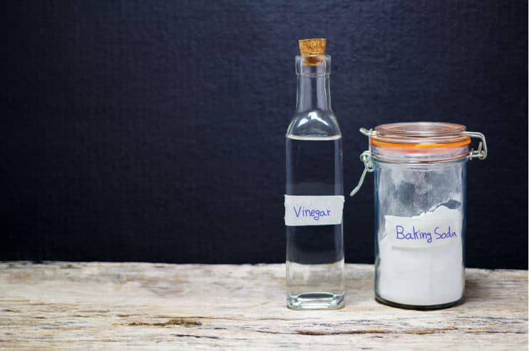 bottle of vinegar and a full jar of baking soda on a wooden bench