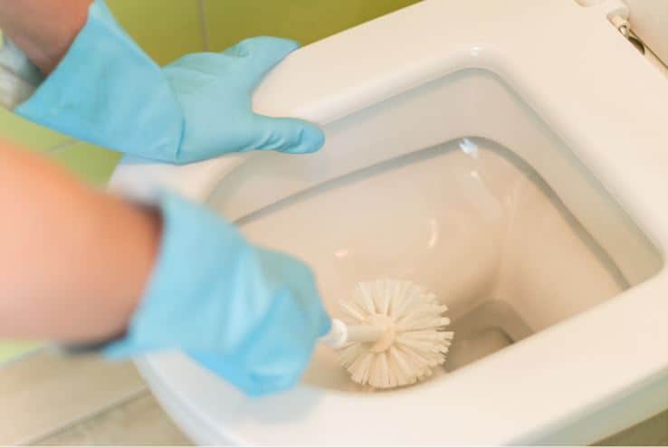 person with blue gloves scrubbing water stained white porcelain toilet