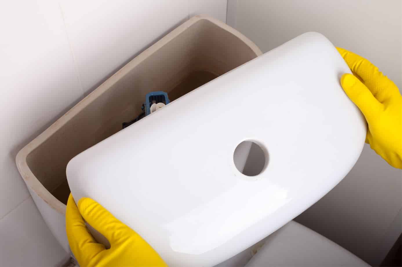 person wearing yellow gloves lifting up lid of toilet tank
