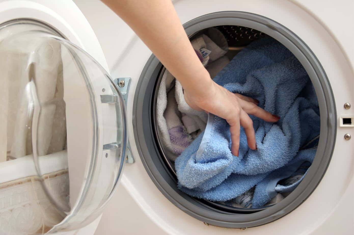 person placing blue bath mat into a full white front loader washing machine