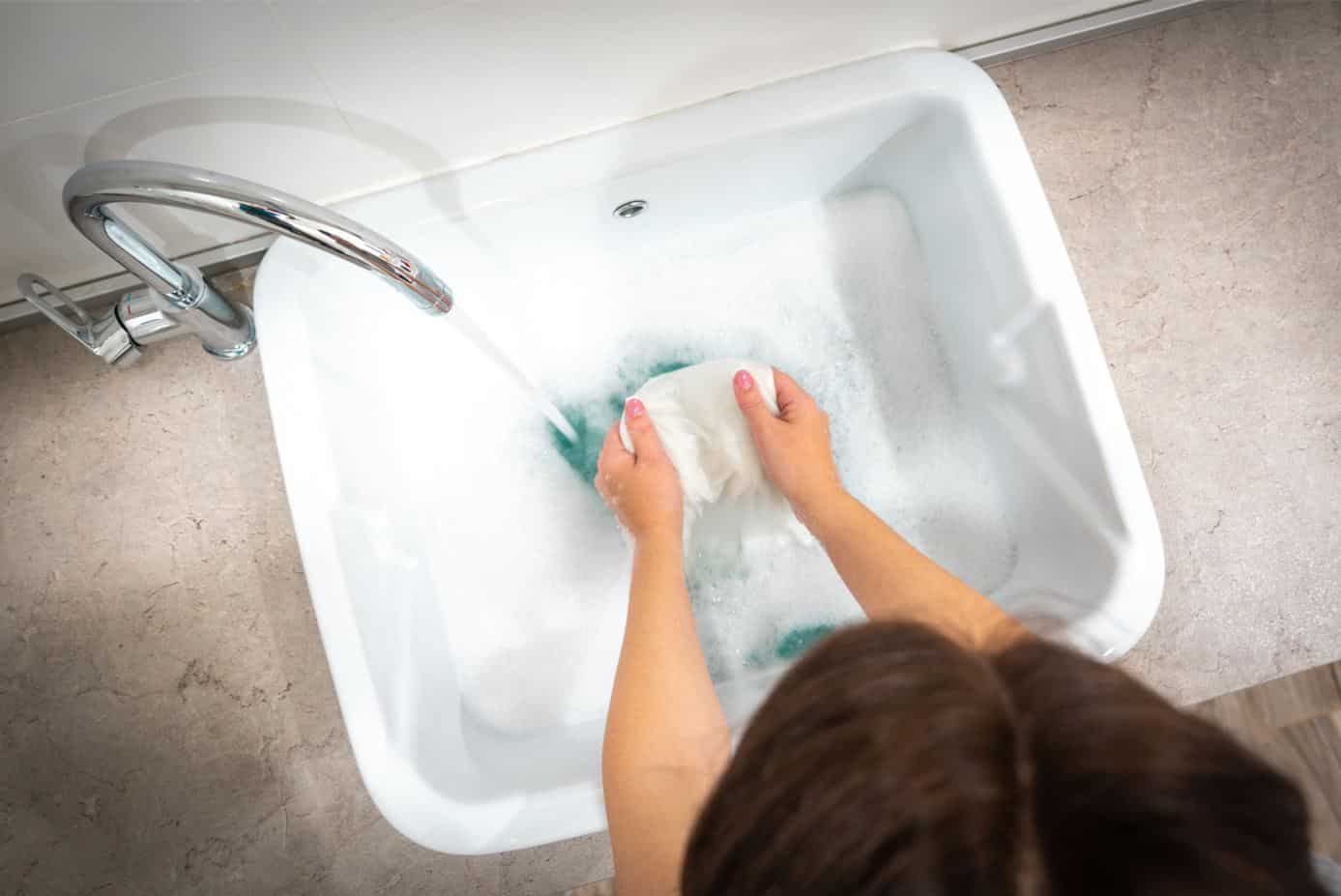 woman using a white basin filled with soapy water to handwash laundry