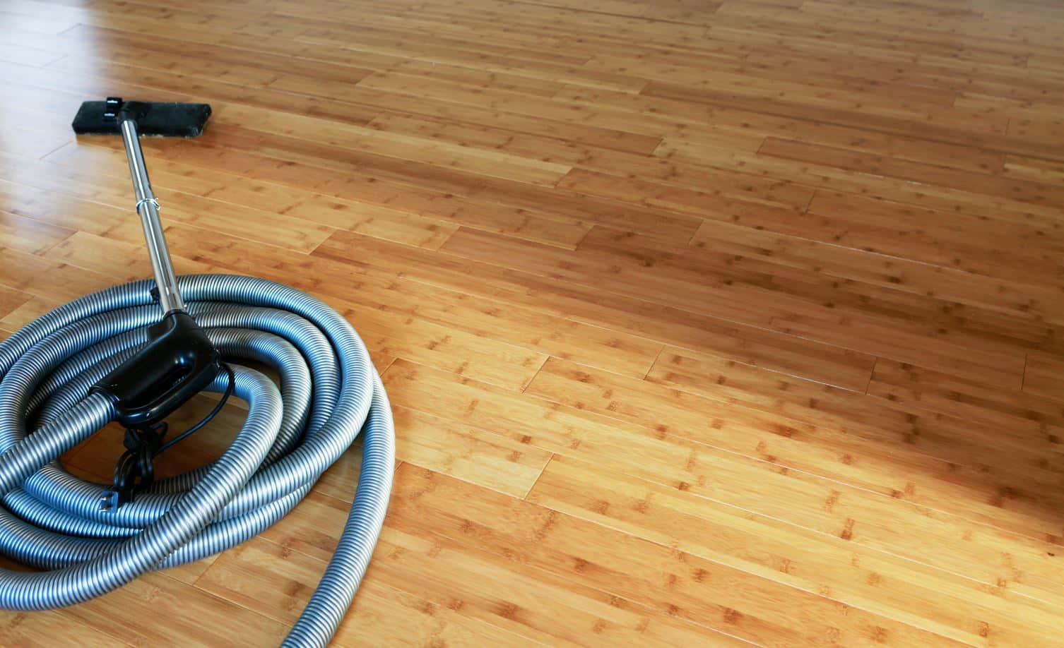 grey vacuum cleaner with black vacuum head on a large light brown bamboo floor