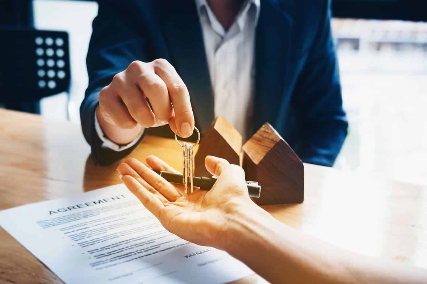seated real estate wearing a blue suit agent passing a set of house keys to a tenant 