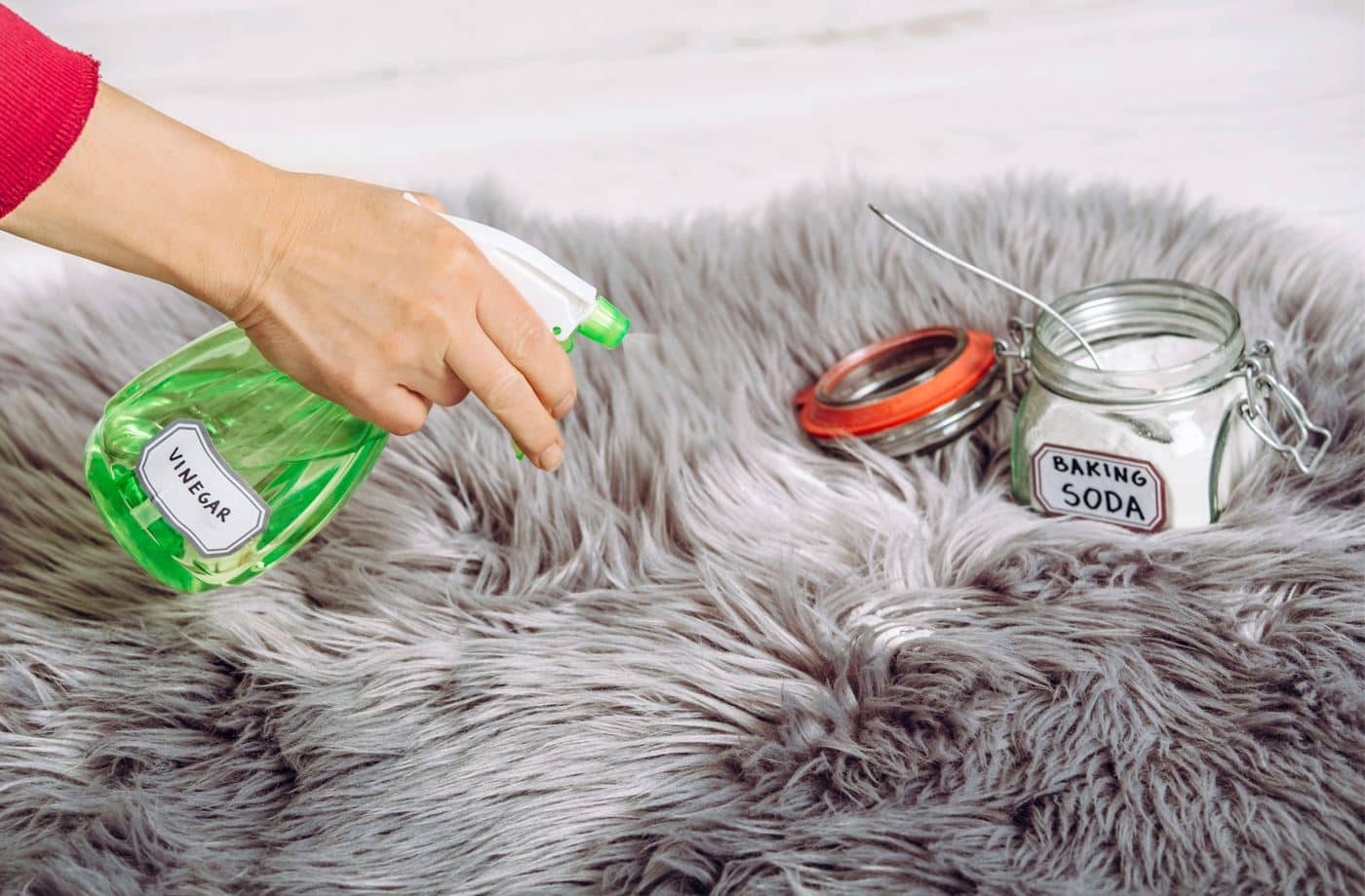woman with green spray bottle of vinegar applying vinegar and baking soda to large grey shag rug