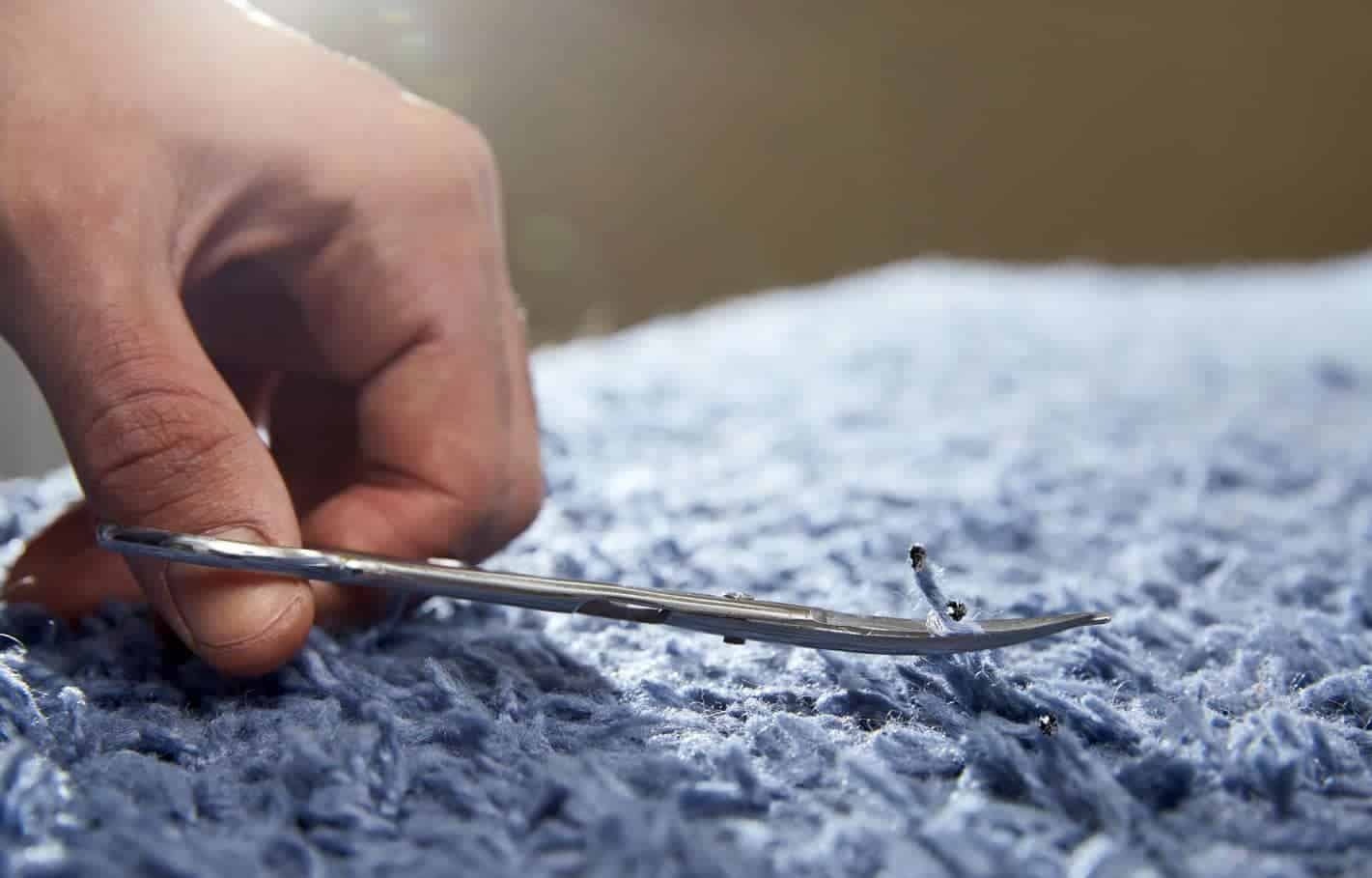 man using scissors to fix carpet burn on blue carpet