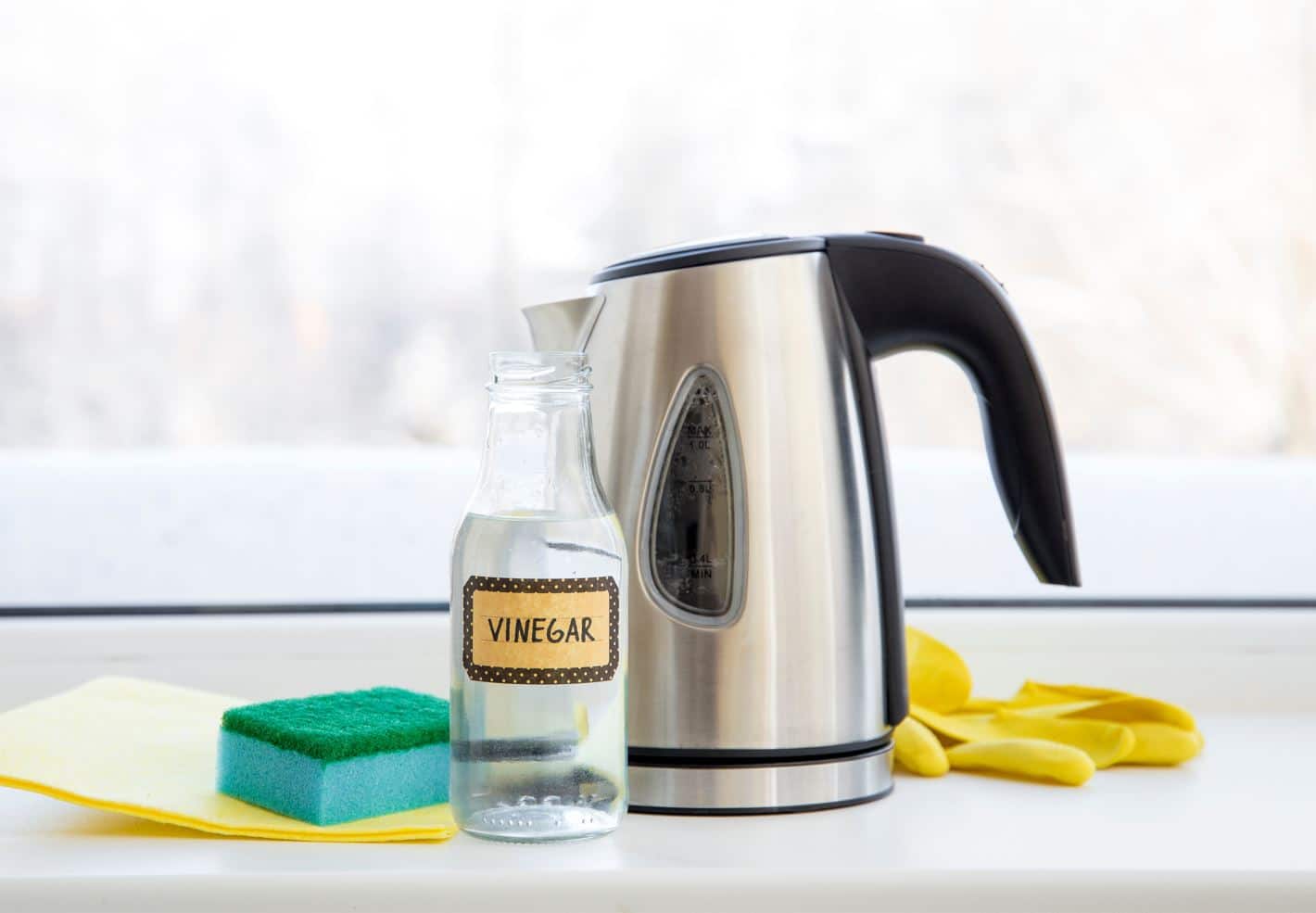 vinegar in a container next to a kettle and cleaning supplies