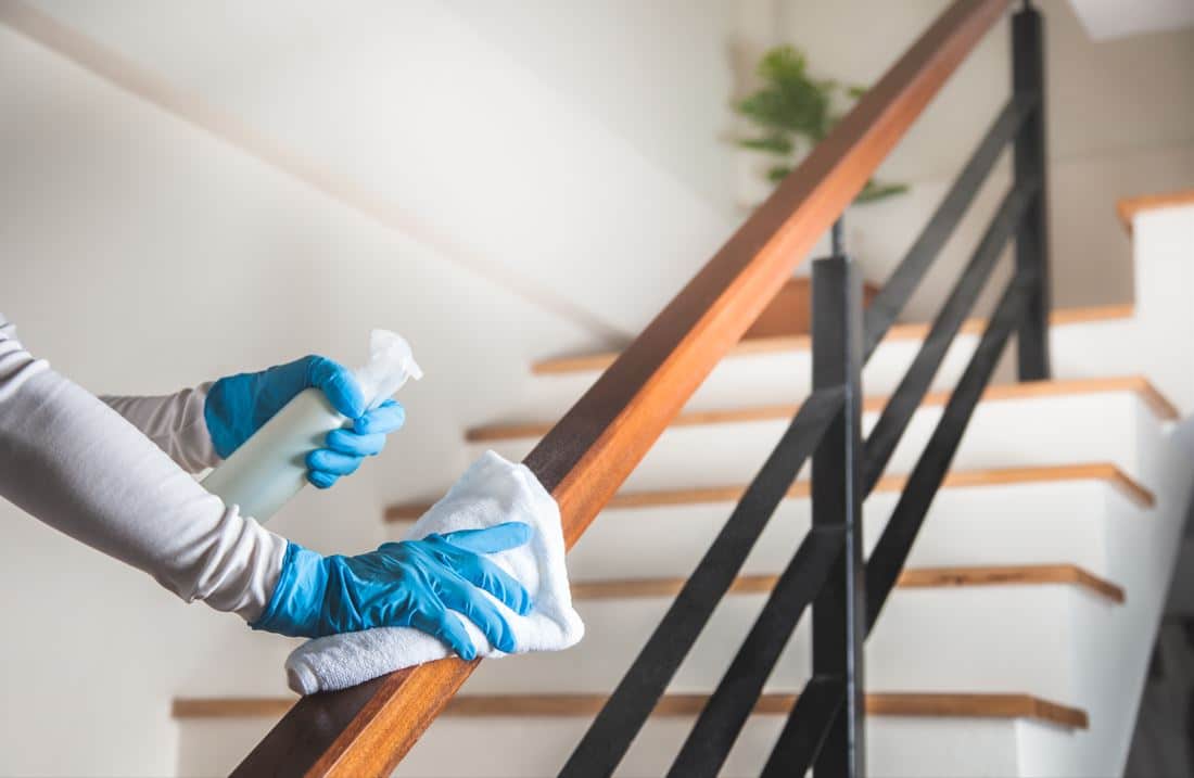 cleaner wearing blue gloves cleaning wooden staircase balustrade