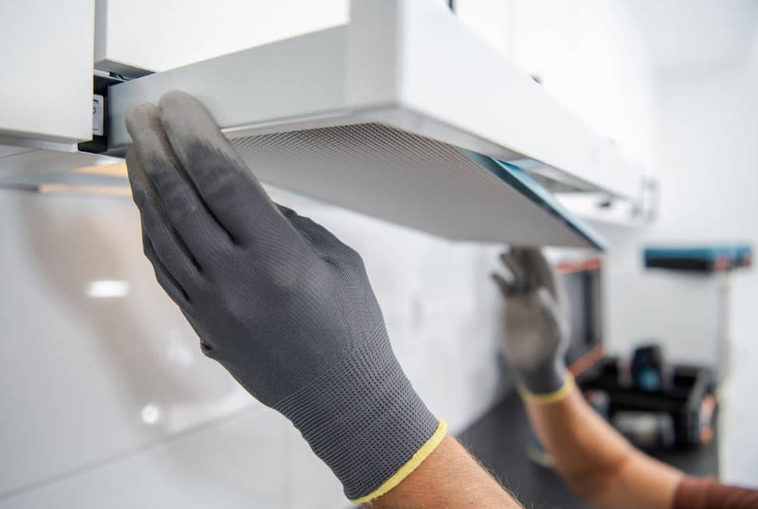 person wearing black gloves putting rangehood filter back in place
